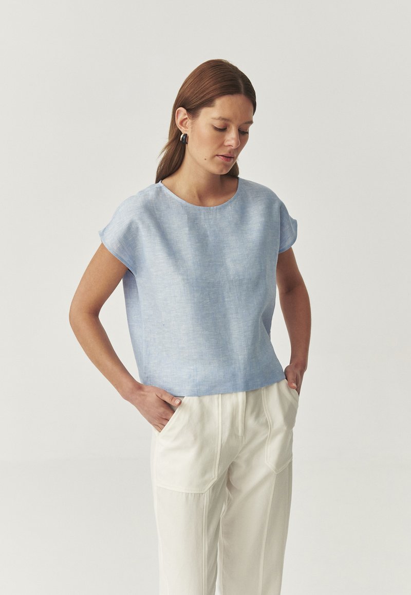 Top azzurro chiaro a maniche corte in lino con vestibilità comoda, scollatura rotonda e finitura testurizzata, abbinato a pantaloni color crema.