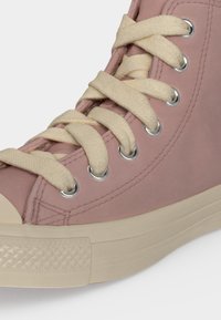 Κοντινό πλάνο ροζ sneaker υψηλής κορυφής με κρεμ χοντρά κορδόνια και μπεζ λαστιχένια σόλα σε ανοιχτό φόντο.