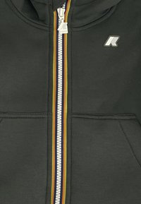 Felpa nera con zip caratterizzata da una cerniera colorata con strisce rosse, gialle e verdi, un piccolo logo sul petto e tasche frontali.