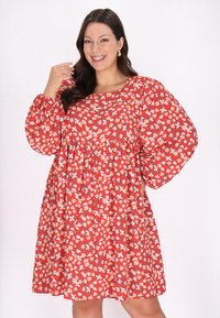 Rochie roșie cu flori, cu mâneci bufante, având o talie strânsă și o croială lejeră. Modelul include diverse flori și frunze în culori crem și pastel.