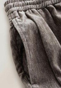 Gros plan sur un pantalon gris en tissu côtelé avec une ceinture élastique et une poche latérale.