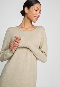 Beige Pullover aus weichem, strukturiertem Material mit weitem Ausschnitt, langen Ärmeln und gerippten Bündchen. Die Passform ist entspannt und leicht oversized.