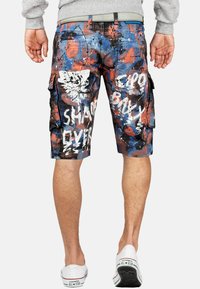 Shorts cargo en tissu multicolore avec un design de éclaboussures de peinture bleues, rouges et blanches, accentués de texte et comportant des poches latérales.