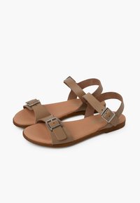 Brown sandals with two wide straps and metallic buckles, featuring a flat sole and soft footbed for comfort.