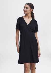Robe noire en tissu léger, avec un décolleté en V, des manches courtes et une coupe décontractée. Jupe fluide avec un lien ajustable.