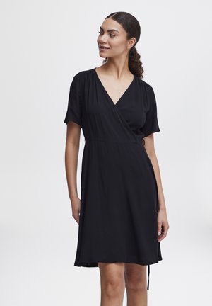 Robe noire en tissu léger, avec un décolleté en V, des manches courtes et une coupe décontractée. Jupe fluide avec un lien ajustable.