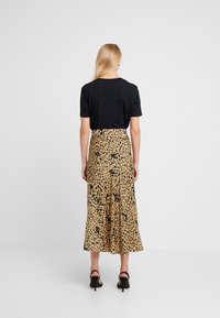 Top nero a maniche corte abbinato a una gonna fluida di lunghezza media, con stampa leopardata in beige e nero, e sandali con tacco.