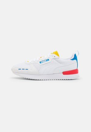 Baskets blanches Puma avec des accents bleus, jaunes et rouges, des panneaux en mesh et cuir, et une semelle texturée, vues de côté.