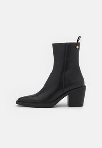Botas de cuero negro hasta el tobillo con punta cuadrada, tacón medio y un botón decorativo dorado en el lateral. Textura suave, diseño elegante.
