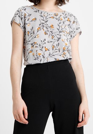 Blusa grigia chiara a maniche corte con un motivo floreale arancione e nero, abbinata a pantaloni neri a vita alta. Texture liscia, vestibilità rilassata.