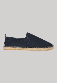 Zapatillas de lona marinas tipo slip-on con suela de yute trenzado, que presentan una sutil etiqueta con el logotipo y paneles laterales elásticos para facilitar su uso.