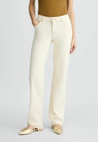 Pantalons en denim blanc à coupe droite, avec poches avant, fermeture à bouton et détails de couture. Assortis à des ballerines dorées claires.