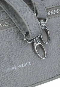 Borsa a tracolla in pelle grigia con texture e accessori in metallo argentato, caratterizzata da doppi dettagli con clip e logo "GERRY WEBER" in rilievo sulla parte anteriore.