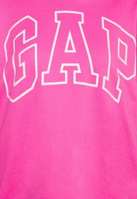 Tejido de un brillante color rosa con letras en negrita y contorno blanco que dicen "GAP" en el centro.