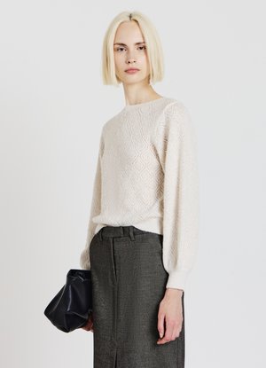 Maglione crema strutturato con motivo a diamante, scollo rotondo e maniche lunghe leggermente gonfie, abbinato a una gonna scura e una borsa nera.