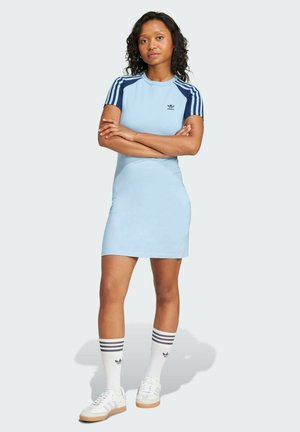 Abito azzurro chiaro con maniche corte, dettagli blu navy e il logo Adidas sul petto. Abbinato a sneakers bianche e calzini a righe.