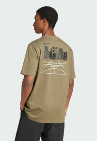 T-shirt in cotone verde oliva con maniche corte e stampa grafica che raffigura uno skyline urbano e un campo da basket sul retro.