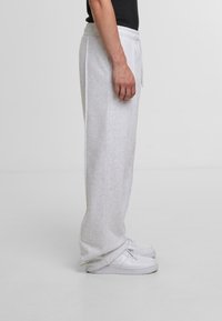 Light gray, knit sweatpants with a relaxed fit, elastic waistband, side pockets, and ribbed cuffs, worn with white sneakers.