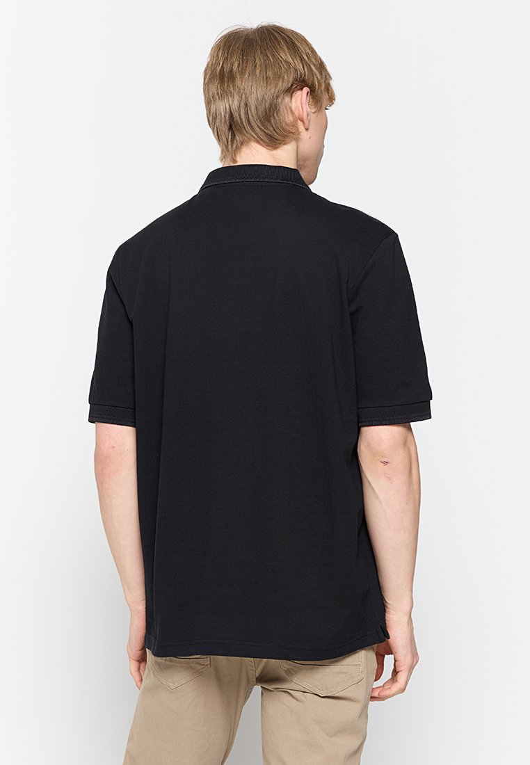 Polo noir à manches courtes, col côtelé et ourlet droit. Fabriqué en coton, il présente une texture lisse avec un minimum de détails.