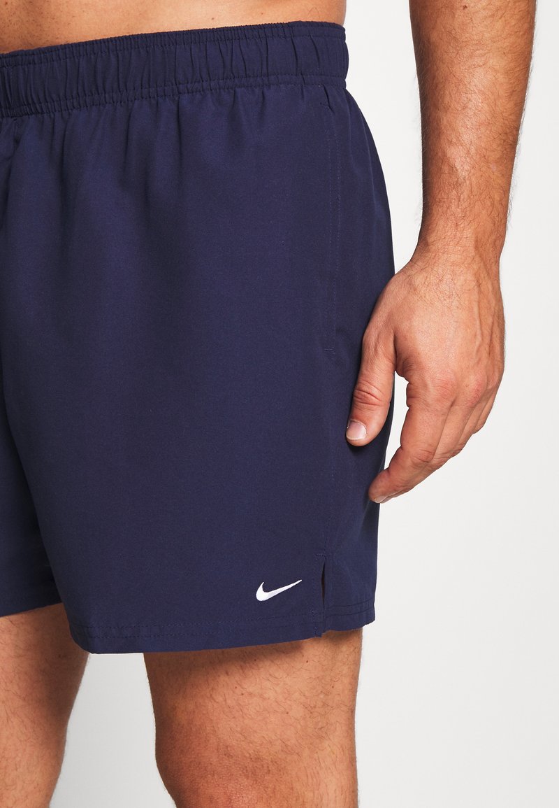 Bañadores de color azul marino con una cintura elástica, bolsillos laterales y un pequeño logo blanco de Nike en la parte inferior izquierda. Textura suave.