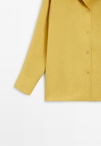 Yellow long-sleeve shirt with buttons down the front and a cuffed sleeve on a white background.
