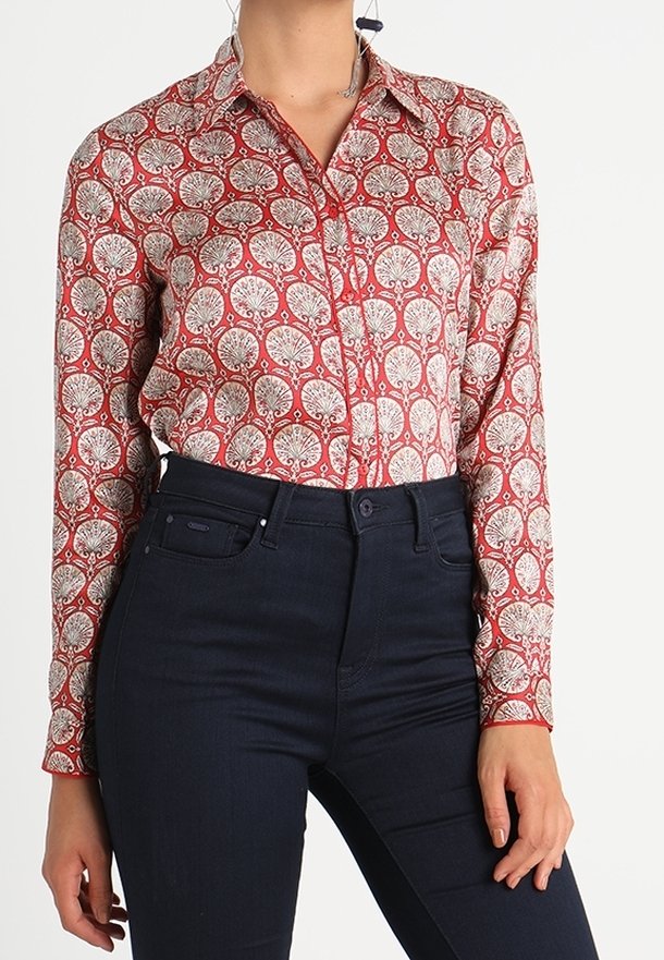 Chemise à motifs boutonnée avec un design d'arbres rouges et crème, manches longues et col, associée à un jean taille haute bleu foncé.
