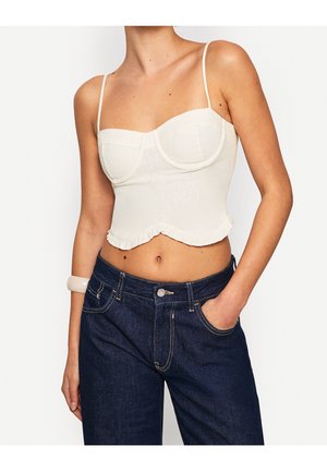Top court blanc avec des bonnets à armatures et un ourlet volanté. Assorti à un jean taille haute bleu foncé. Tissu lisse, fines bretelles.