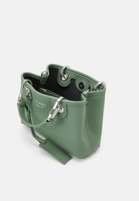 Zielona torebka skórzana o fakturze z metalowymi elementami w kolorze srebrnym, otwarta u góry, z dwoma uchwytami i małą odczepianą metką. Wnętrze wykończone czarną podszewką.
