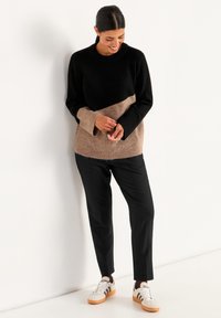Stickad tröja med svart och beige färgblockdesign, ribbade muddar, kombinerad med svarta byxor och vita sneakers med bruna detaljer.