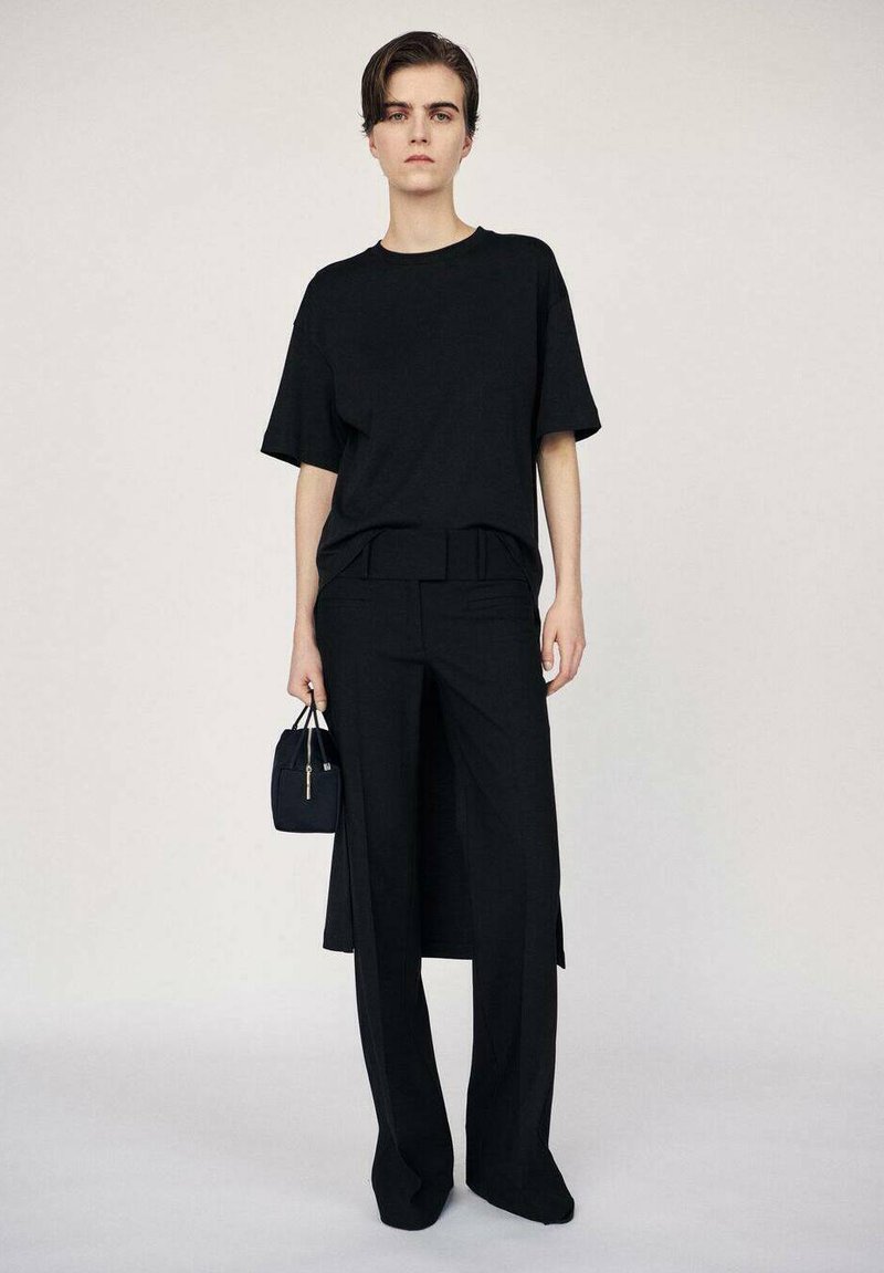 T-shirt noir surdimensionné à manches courtes, associé à un pantalon noir taille haute. La tenue présente un design minimaliste et une texture lisse.