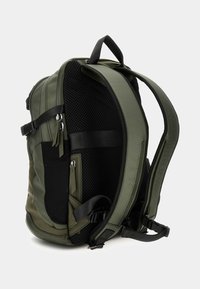 Sac à dos vert olive avec panneau en maille et poches zippées. Bretelles réglables et design structuré, avec un mélange de tissus lisses et texturés.