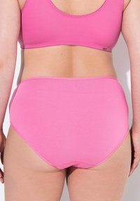 Slip di cotone rosa con vita alta e texture liscia. Presenta un design semplice con cuciture minime lungo i bordi.