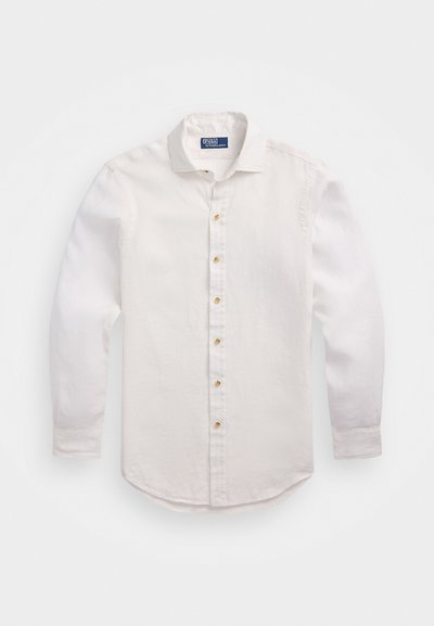 Λευκή μακριά μπλούζα με μανίκια από ελαφρύ ύφασμα. Διαθέτει κουμπί μπροστά, κλασικό γιακά και στρογγυλή ασύμμετρη γραμμή στο τελείωμα. Χρυσά κουμπιά προσθέτουν στυλ στο μπροστινό μέρος.