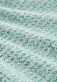 Een gestructureerde, gebreide stof in licht muntgroen met subtiele blauwe vlekken, die een zachte, fuzzy uitstraling en golvend patroon heeft.