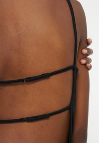 Κοντινό πλάνο του πάνω μέρους της πλάτης ενός ατόμου που φοράει ένα μαύρο ρούχο με λουράκια, με το δεξί του χέρι να κρατάει τον αριστερό ώμο.