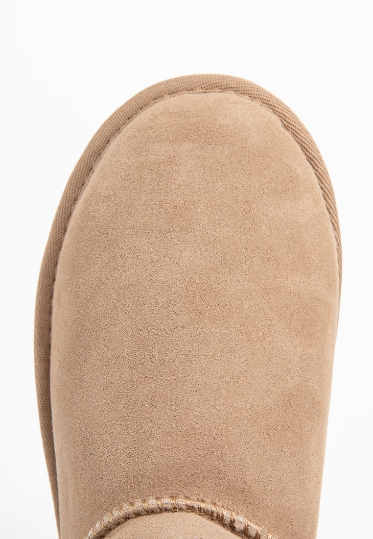Beżowy zamszowy but z okrągłym noskiem, widocznym szyciem wzdłuż krawędzi i teksturowanym materiałem po bokach dla lepszej przyczepności.