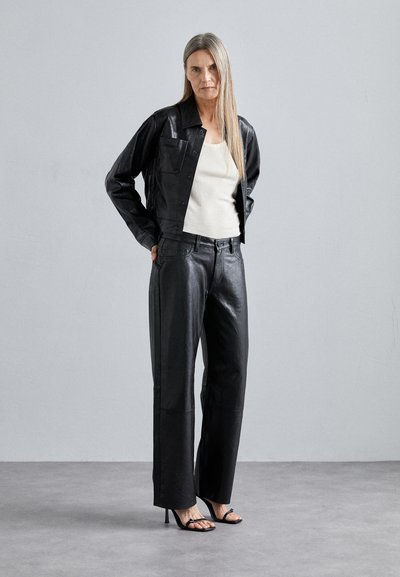 Black leather jacket and matching trousers, with a textured finish and tailored fit. Paired with a light tank top and black heeled sandals.
