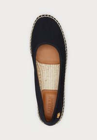 Zapato plano de lona azul marino con punta redondeada, plantilla de cuero, suela de yute y detalles de borde tejido. Acento de logo dorado cerca del talón.