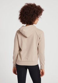 Sweatshirt beige à capuche avec une texture douce et des manches raglan. Les poignets et le bas sont ajustés, associés à des leggings noirs élégants.