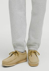 Beige nubuck sko med en rund tådesign, snøret med tynde snørebånd, parret med lysegrå sweatpants med elastiske manchetter.