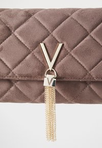 Θησαυροφυλάκιο από σουέτ σε απόχρωση καφέ με πικές σχεδιάσεις και χρυσό λογότυπο σε σχήμα V, καθώς και λεπτομέρεια από κρεμαστή αλυσίδα. Μαλακή υφή με γεωμετρικό σχέδιο.