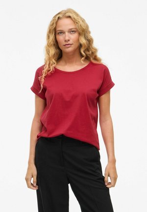 Maglietta rossa a maniche corte in cotone, con scollatura rotonda, vestibilità rilassata, abbinata a pantaloni neri. Tessuto liscio con orli delle maniche piegati.