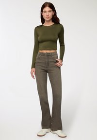 Zielony, długi rękaw crop top w połączeniu z szarymi, wysokim stanem, rozszerzającymi się dżinsami i białymi trampkami. Gładka tkanina i dopasowany krój podkreślają sylwetkę.