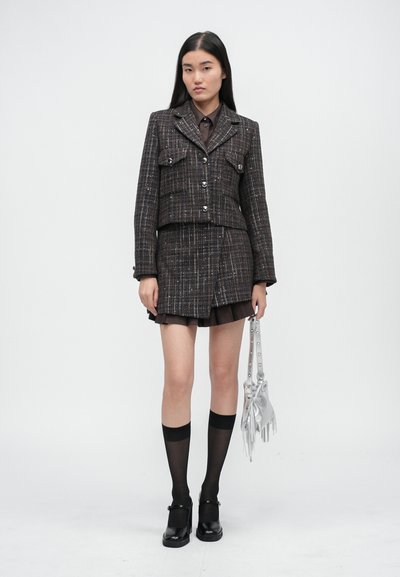Tweed jakk koos kahe ees pocketiga, nööbilukuga, millele on sobitatud mini seelik. Aksessuaarideks on hõbedane kott ja kuni põlvedeni ulatuvad mustad sokid.