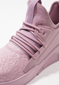 Lila sportskor med texturerad ovandel, platta skosnören och en förstärkt sula med kantiga designelement. Reebok-märkning på tungan.