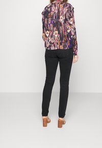 Blusa de flores de manga larga en tonos de púrpura, rosa y crema; con hombros con volantes; combinada con pantalones ajustados negros y sandalias de tacón marrones.