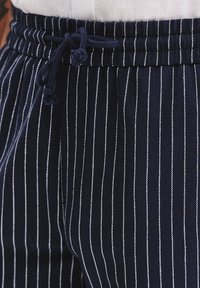 Granatowe spodnie w paski z elastycznym pasem, z pionowymi białymi prążkami i miękką teksturą materiału.