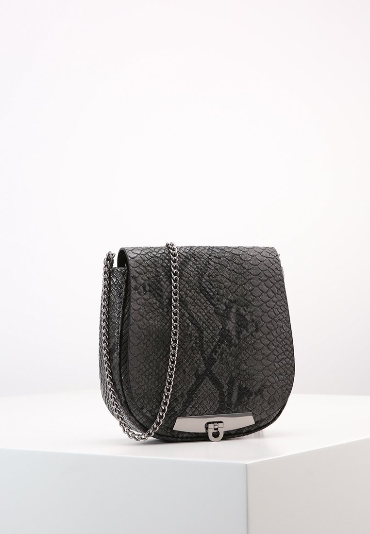 Mustan tekonahkaisen käärmeenahkakuvioidun olkalaukun kaareva siluetti, hopeaketjuside ja metallinen lukon yksityiskohta. Pinta on teksturoitu ja lisää syvyyttä.