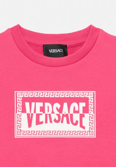 Erksav roosa ümara kaelusega pusa, millel on ees valge Versace logo ja Kreeka võtme ääris, kaelas sees must Versace silt.