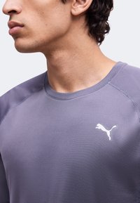 Νέος/Νέα με πορφυρό αθλητικό πουκάμισο Puma που δείχνει το πάνω μέρος του στήθους και το πλάι του προσώπου και του λαιμού.